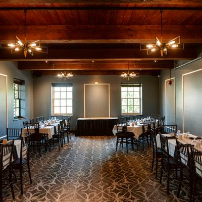 Interior featuring long dining tables, wooden ceiling beams and geometric chandeliers.