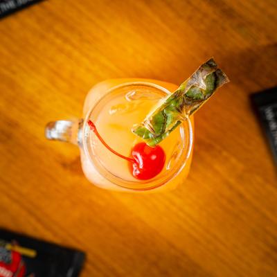 Juicy Rum Punch served in a mason jar, garnished with a pineapple wedge and a cherry.