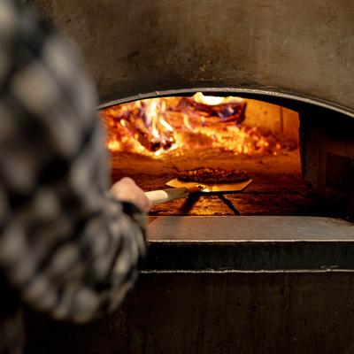 A pizza maker holding a peel with a pizza inside a pizza oven.