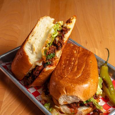 A Mexican torta sandwich, cut in half to show chorizo filling and cheese, served on a metal tray.