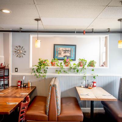 Diner interior with tables, cushioned booths, and chairs, green plants adorn a wall shelf.