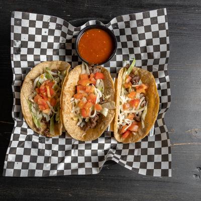 Tacos served on checkered deli paper with a small cup of red salsa.