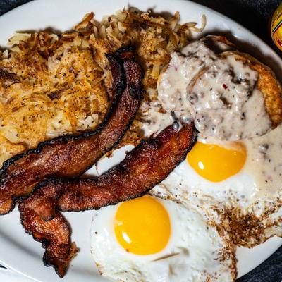 Breakfast plate with eggs, bacon, hash browns and a biscuit.