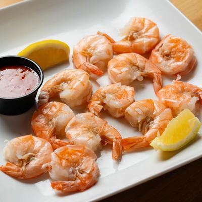 Peel & Eat Boiled Shrimp served with a red sauce and lemon wedges.