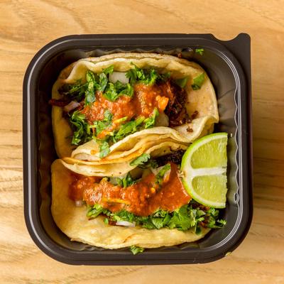 Tacos with cilantro, salsa, and a lime wedge in a takeout container.