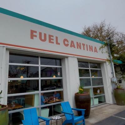 Exterior of Fuel Cantina with large windows, blue chairs, and large potted plants.
