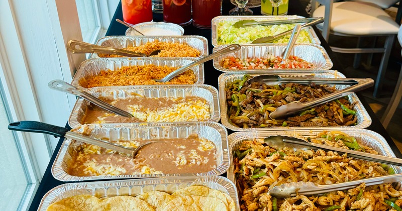 Buffet setup with trays of rice, beans, and fajitas
