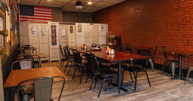 Interior of a dining area with wooden tables, metal chairs, and a red brick wall