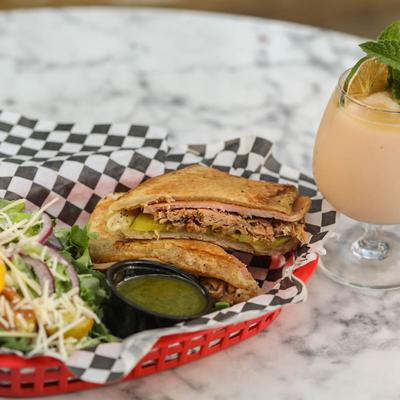 Pulled pork sandwich served with a salad and a cocktail.