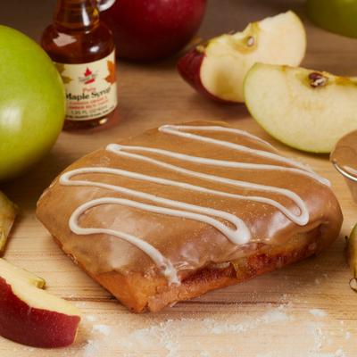 Apple-filled pastry with maple glaze and white icing on a wooden board with sliced apples.