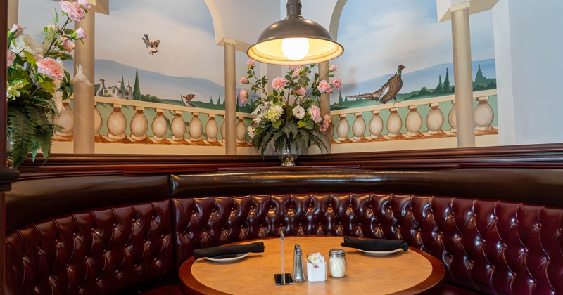 Restaurant booth with maroon seating and mural of a terrace view with arches