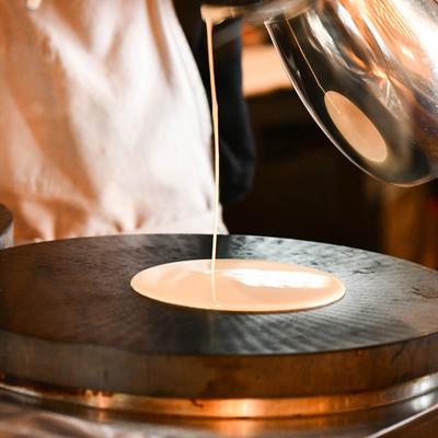 A person pouring crepe batter on a round griddle.