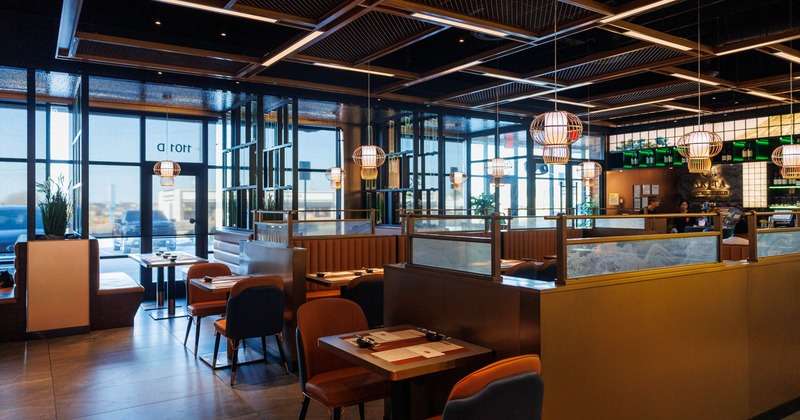 A modern restaurant interior with wooden furnishings, pendant lighting, and large windows