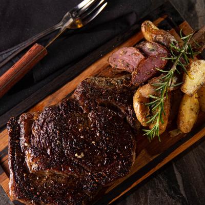 Char-grilled rib eye steak on a wooden board with sweet potatoes