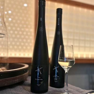 Two tall dark bottles of sake alongside a filled wine glass on a table.