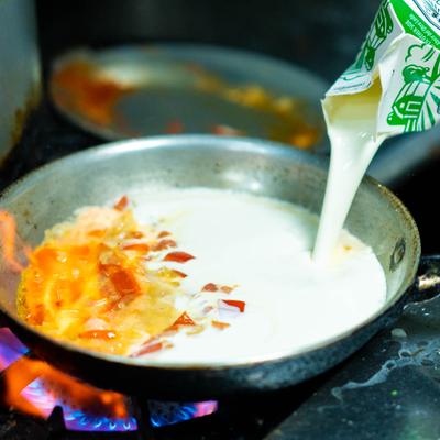 Chef pouring cream in the pan.