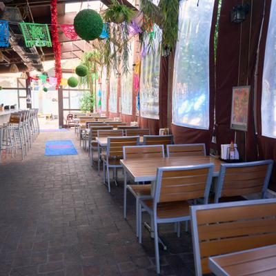 Covered outdoor dining area with hanging plants and wooden tables.