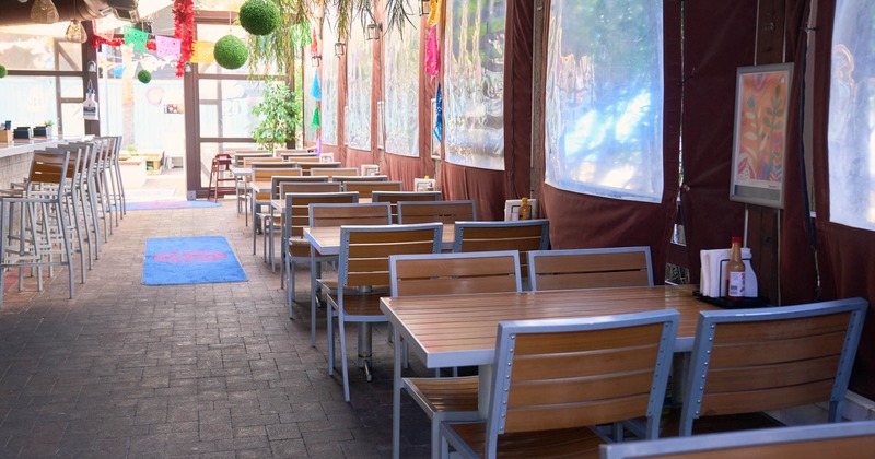 Covered outdoor dining area with hanging plants and wooden tables