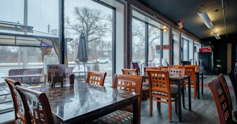 Interior of a restaurant with large windows showing a snowy landscape outside, wooden tables, and chairs inside.