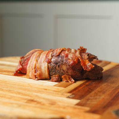 Bacon-wrapped meatloaf served on a wooden cutting board.