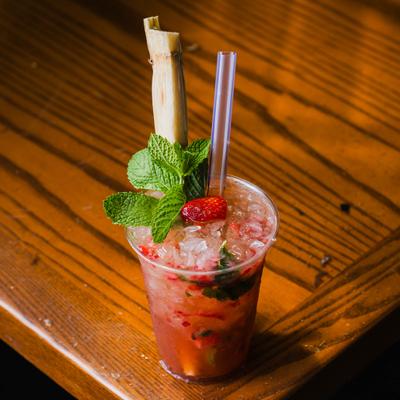 Strawberry mojito served in a plastic cup with a sugarcane stalk garnish.