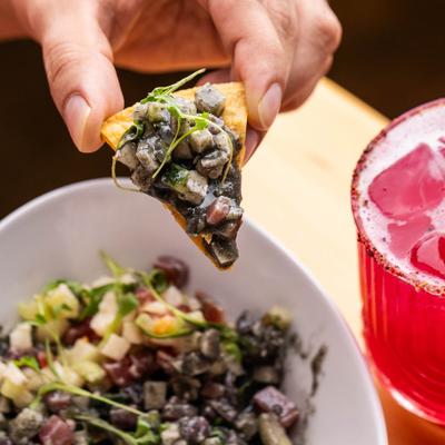 A hand holding a tortilla chip topped with black ceviche.