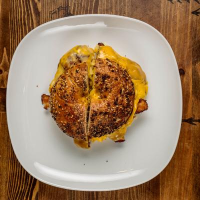 Breakfast sandwich featuring bacon, egg, and cheese, served on a toasted everything bagel.