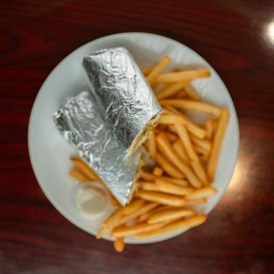 Foil-wrapped shawarma sandwich with fries on a white plate.