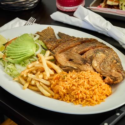 A whole fried fish served with orange rice, french fries, and avocado.