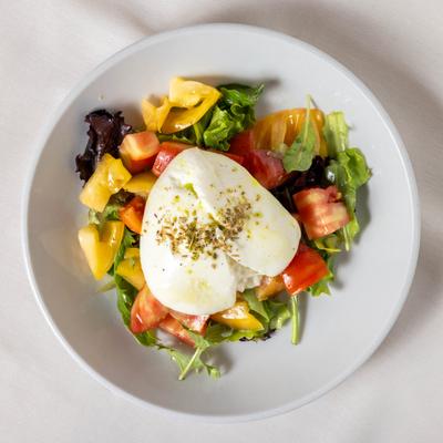 Burrata served over a bed of greens with organic tomatoes, and lemon oregano dressing.