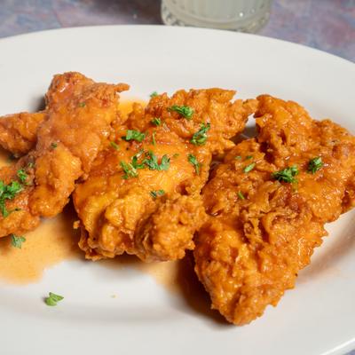 Buffalo Chicken Fingers garnished with herbs, alongside a cocktail.