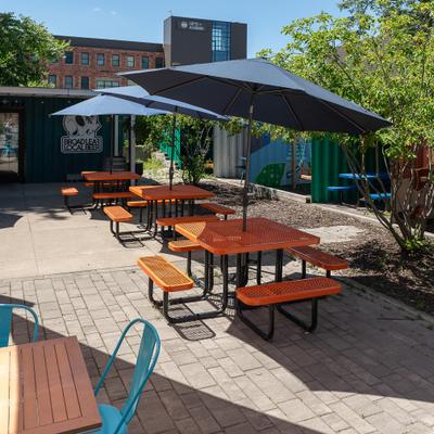 Outdoor patio seating featuring picnic tables shaded by a large umbrella.