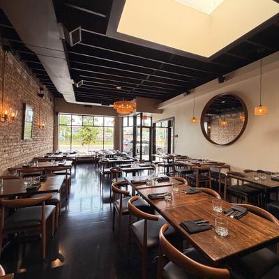 Restaurant dining room with wooden tables, exposed brick walls, mirrors, and pendant lights.