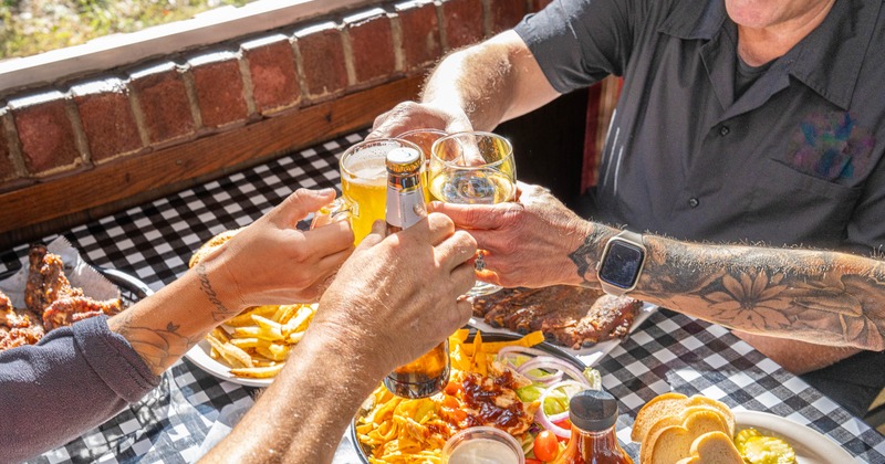 Hands from multiple guests making a group toast with drinks over a full table