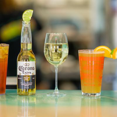 Cocktail drinks, a glass of white wine, and a bottle of beer lined on a bar counter.
