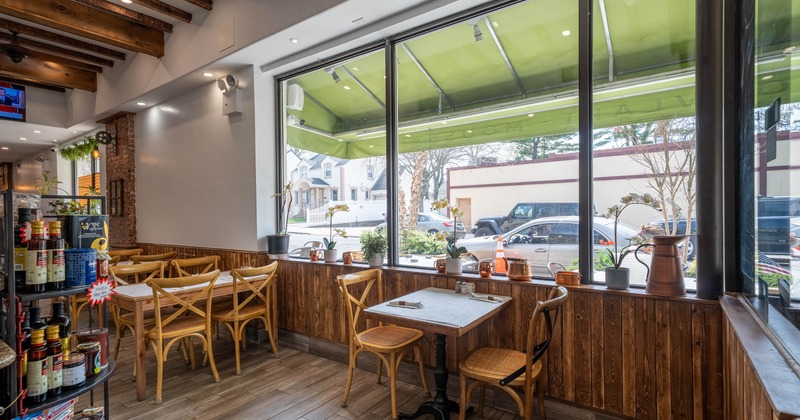 Interior of a cafe with wooden decor, large windows, tables, chairs, and shelves with food items