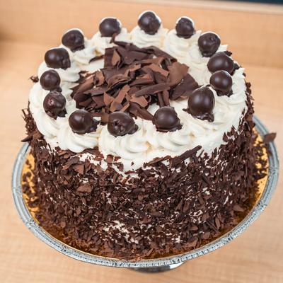 Cake decorated with chocolate shavings, whipped cream, and chocolate-covered cherries.