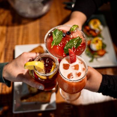 Three people raising their glasses in a toast above food plates on a table, top view.