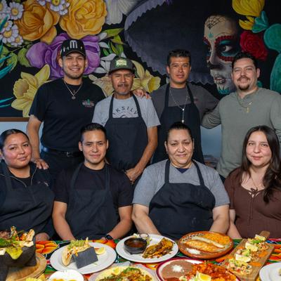Restaurant staff posing together at a table with assorted Mexican dishes.