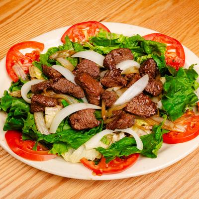 Shaken Steak served over mixed greens with onions, tomato, and a lemon dipping sauce.