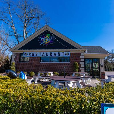 Exterior with signage, outdoor seating, and greenery against a clear blue sky.