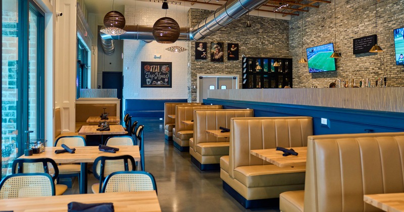 A modern interior - wooden tables, tan upholstered booths, large windows.