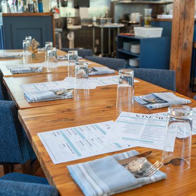 Closeup on a set up wooden top tables with menus, cutlery and glasses.