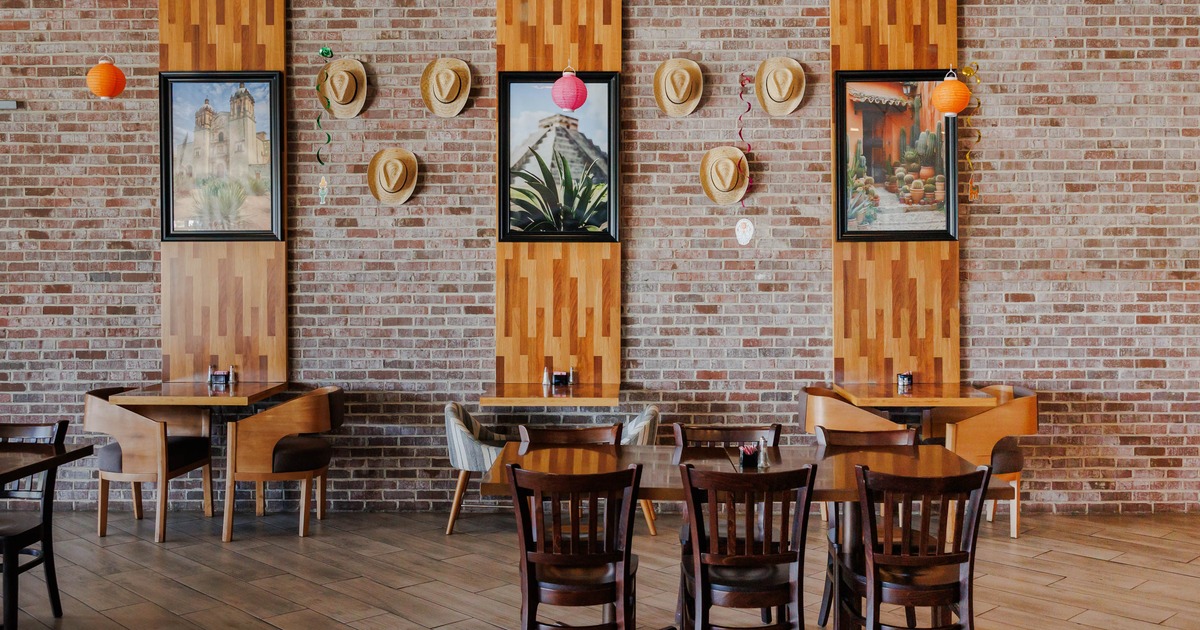 Restaurant interior with brick walls, wooden panels with framed art, straw hats