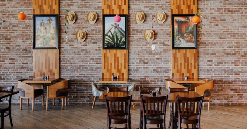 Restaurant interior with brick walls, wooden panels with framed art, straw hats