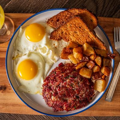 Two sunny side up eggs, sausage patty, breakfast potatoes, and toast, top view.