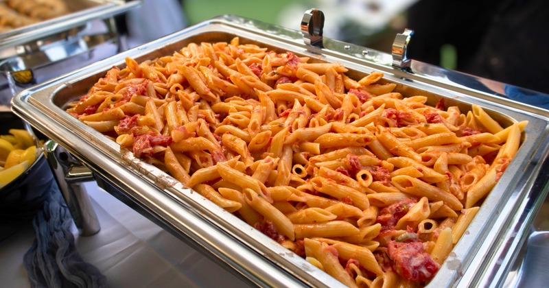 Penne pasta with a creamy tomato sauce being served in a chafing dish