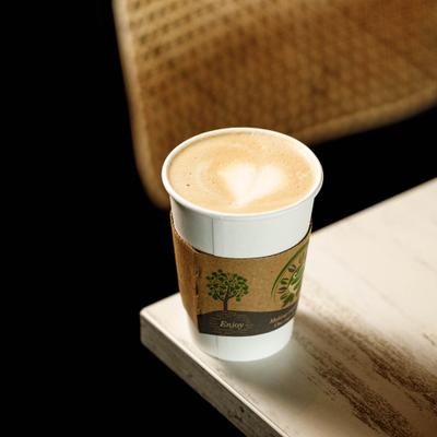 A white paper coffee cup with cappuccino on a wooden table.
