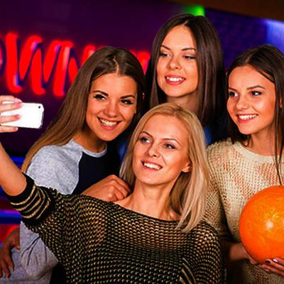 Four friends smiling while taking a selfie in a dimly lit bowling alley.