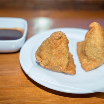 Two samosas with sauce in the background.